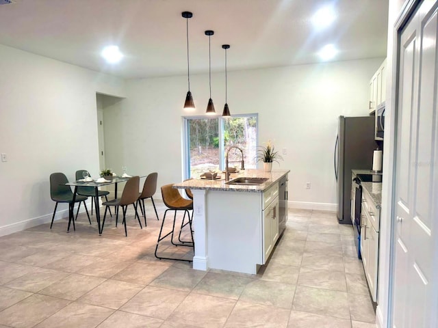 kitchen featuring sink, appliances with stainless steel finishes, white cabinetry, light stone countertops, and an island with sink