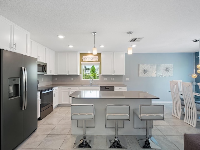 kitchen featuring stainless steel appliances, a sink, white cabinetry, a kitchen bar, and a textured ceiling