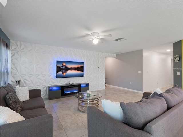 tiled living area with an accent wall, baseboards, ceiling fan, wallpapered walls, and a glass covered fireplace