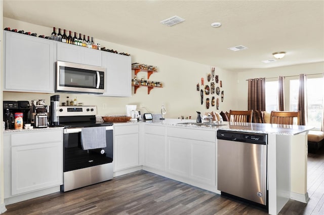 kitchen with appliances with stainless steel finishes, sink, kitchen peninsula, white cabinetry, and dark hardwood / wood-style floors