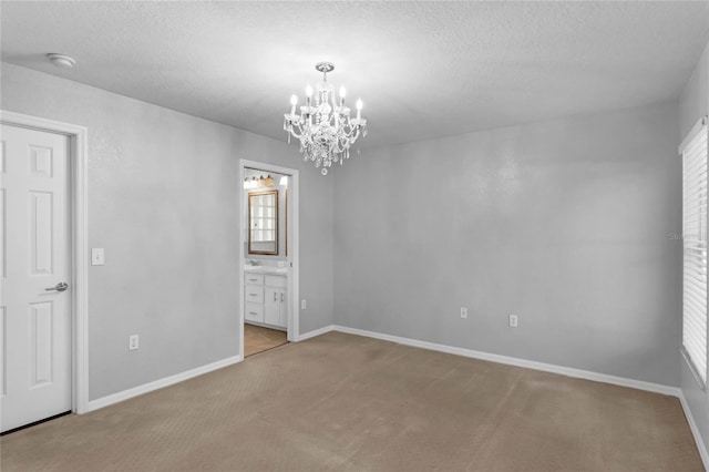 unfurnished room with a textured ceiling, a notable chandelier, and light colored carpet