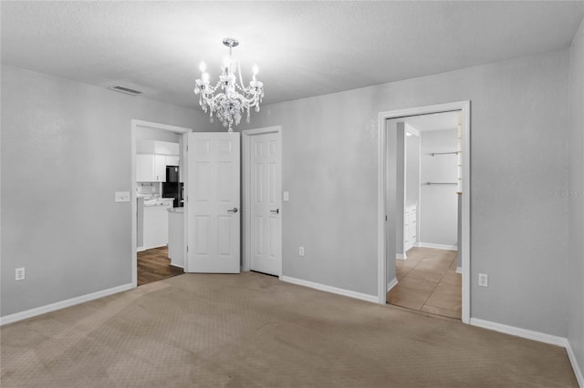 spare room with a textured ceiling, carpet flooring, and an inviting chandelier