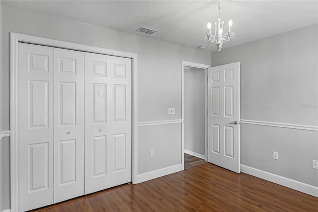 unfurnished bedroom with a notable chandelier, dark hardwood / wood-style floors, and a closet