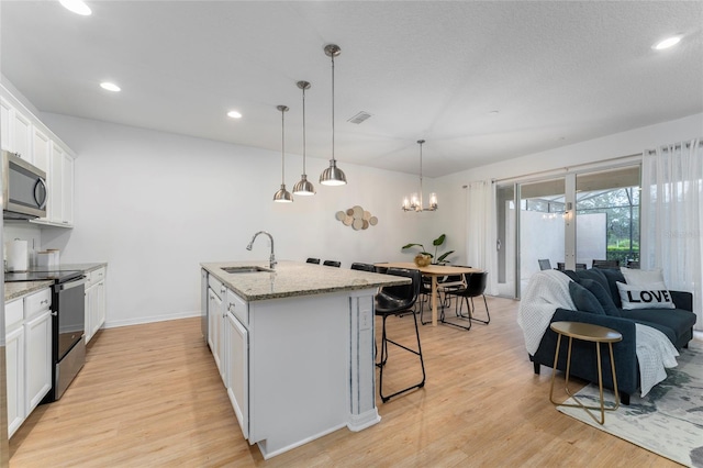 kitchen with black range with electric cooktop, a center island with sink, sink, white cabinetry, and light hardwood / wood-style floors