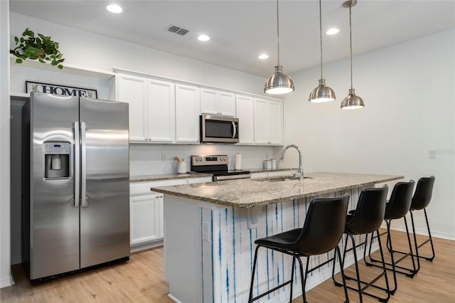 kitchen with appliances with stainless steel finishes, white cabinets, sink, and a center island with sink