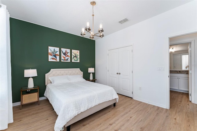 bedroom featuring an inviting chandelier, connected bathroom, light hardwood / wood-style flooring, and a closet