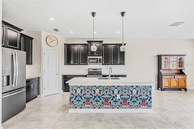 kitchen featuring an island with sink, appliances with stainless steel finishes, a textured ceiling, pendant lighting, and sink