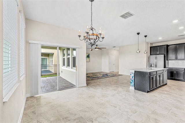 kitchen with ceiling fan with notable chandelier, stainless steel fridge with ice dispenser, pendant lighting, and a center island with sink