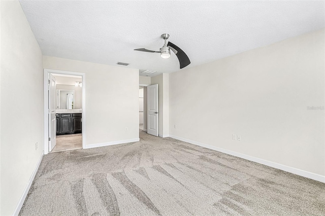 unfurnished bedroom with a textured ceiling, ensuite bathroom, light colored carpet, and ceiling fan