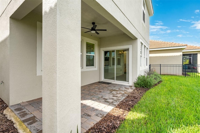 view of exterior entry featuring a patio, a lawn, and ceiling fan