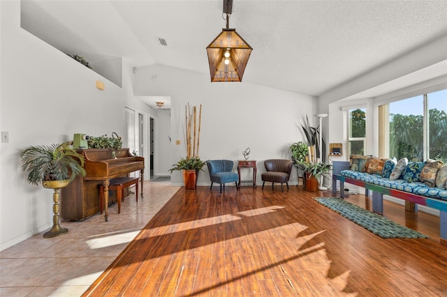 sitting room with a textured ceiling, light tile patterned floors, and vaulted ceiling