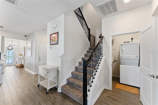 staircase featuring stacked washing maching and dryer, hardwood / wood-style flooring, a textured ceiling, and an inviting chandelier