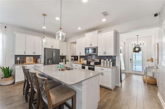 kitchen featuring appliances with stainless steel finishes, white cabinets, decorative light fixtures, and a center island with sink