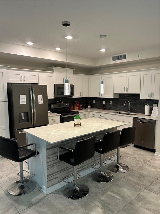 kitchen featuring tasteful backsplash, sink, white cabinetry, stainless steel appliances, and decorative light fixtures