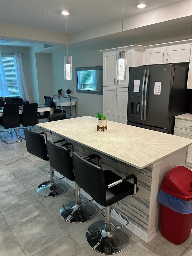 kitchen with a wealth of natural light, stainless steel fridge, white cabinetry, and pendant lighting