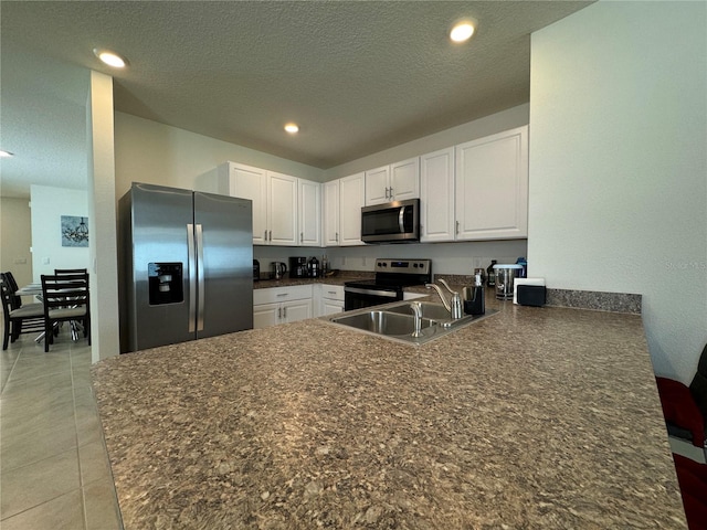 kitchen with kitchen peninsula, stainless steel appliances, sink, white cabinets, and a textured ceiling