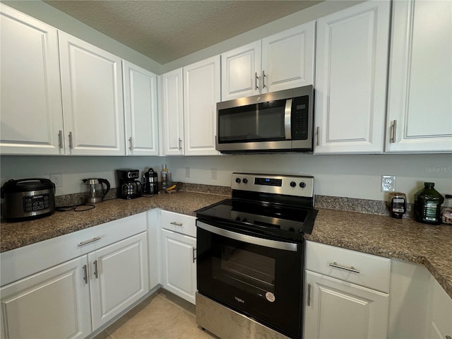 kitchen featuring appliances with stainless steel finishes, a textured ceiling, white cabinetry, and light tile patterned floors