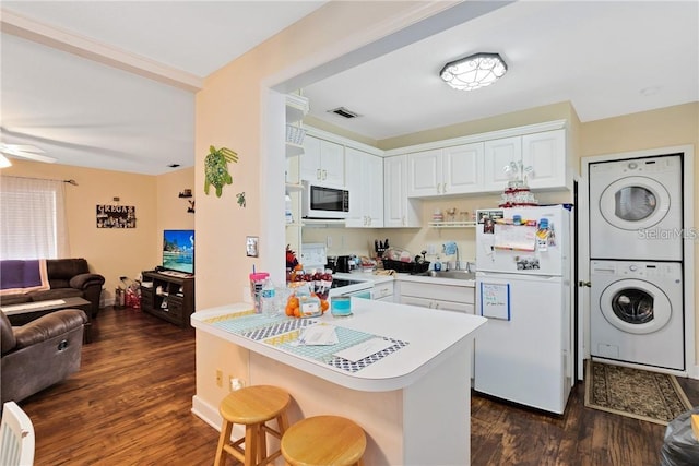 kitchen featuring kitchen peninsula, white cabinets, a breakfast bar, stacked washing maching and dryer, and white appliances