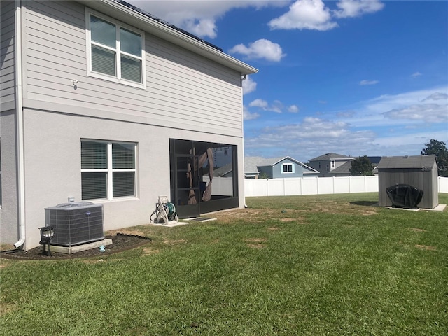 back of property with a lawn, central AC, and a storage shed