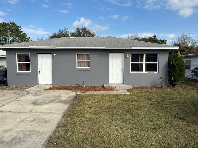 view of front of house with a shingled roof, a front yard, and stucco siding