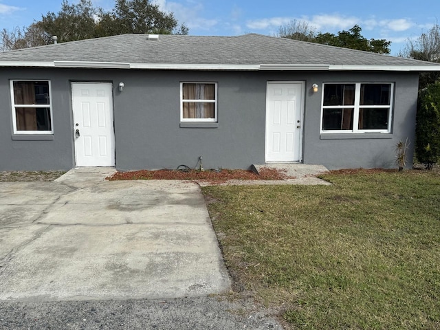 view of front facade with a patio, a front lawn, roof with shingles, and stucco siding