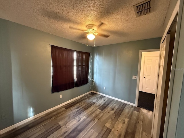 unfurnished bedroom featuring visible vents, a ceiling fan, a textured ceiling, wood finished floors, and baseboards