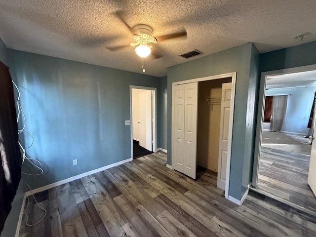 unfurnished bedroom with a closet, visible vents, a textured ceiling, wood finished floors, and baseboards