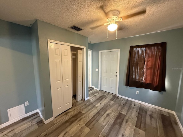 unfurnished bedroom with a closet, visible vents, baseboards, and wood finished floors