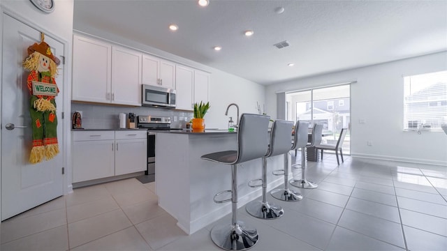 kitchen featuring white cabinetry, appliances with stainless steel finishes, a kitchen island with sink, and a breakfast bar