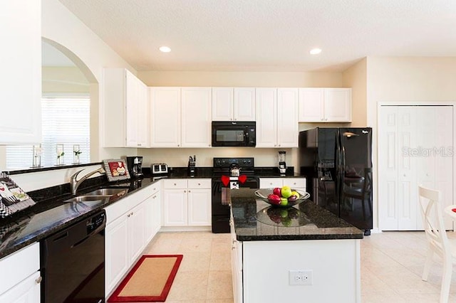 kitchen with white cabinets, light tile patterned flooring, black appliances, sink, and a center island