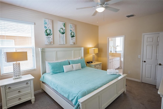 bedroom with multiple windows, connected bathroom, dark carpet, and ceiling fan