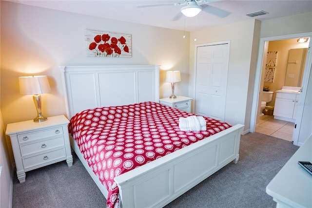 bedroom with a closet, ceiling fan, ensuite bathroom, and dark colored carpet