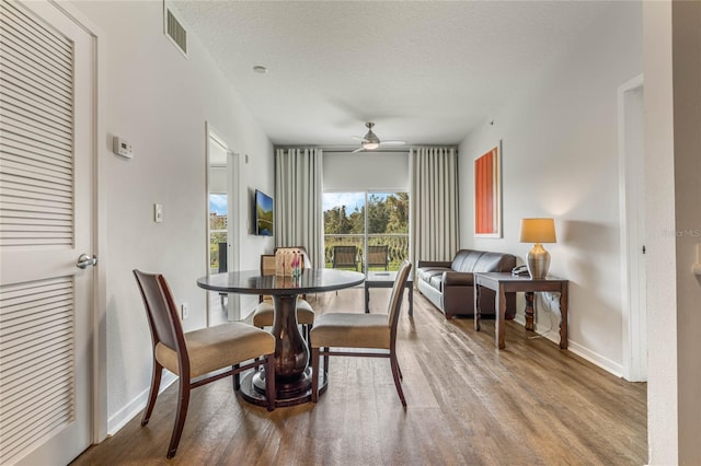 dining room with ceiling fan, visible vents, baseboards, a textured ceiling, and wood finished floors