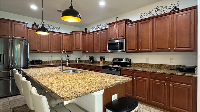 kitchen featuring an island with sink, stainless steel appliances, sink, a kitchen bar, and pendant lighting