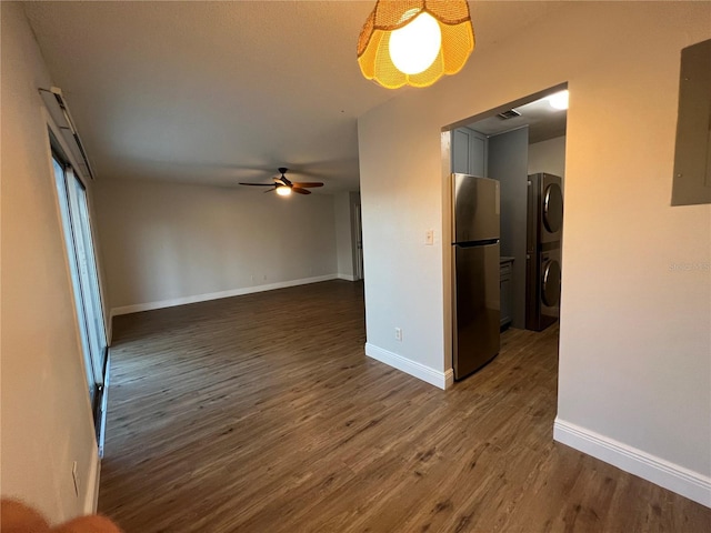 unfurnished living room with stacked washer and clothes dryer, ceiling fan, dark wood-style floors, and baseboards