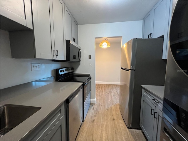 kitchen with gray cabinetry, stainless steel appliances, sink, pendant lighting, and light hardwood / wood-style floors