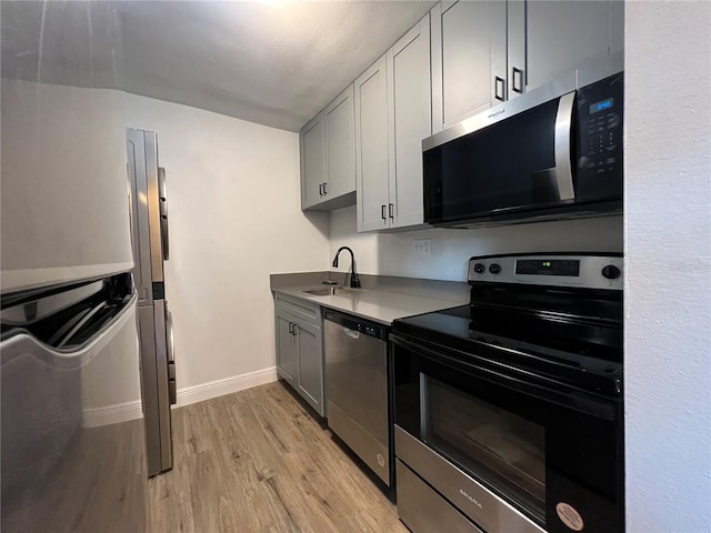 kitchen featuring appliances with stainless steel finishes, a sink, light wood-style floors, baseboards, and gray cabinets