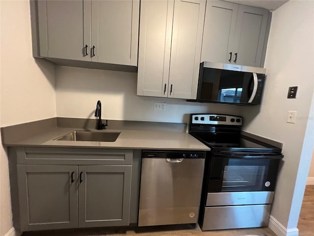 kitchen with stainless steel appliances, a sink, gray cabinetry, and baseboards