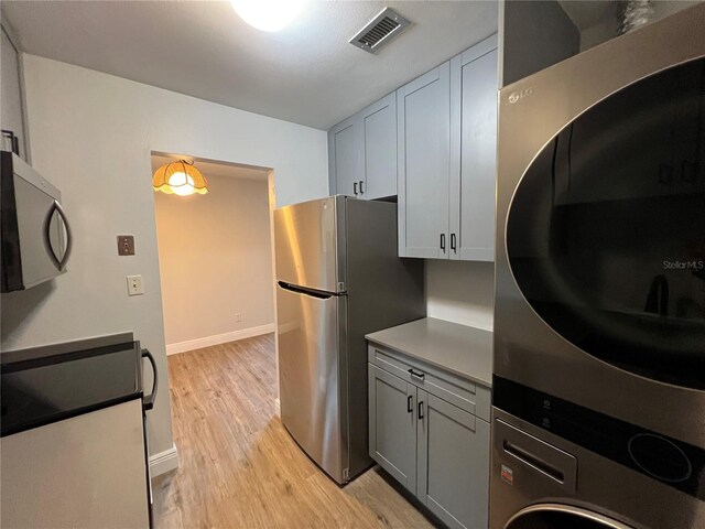 kitchen featuring estacked washer and dryer, light wood-type flooring, freestanding refrigerator, baseboards, and stove