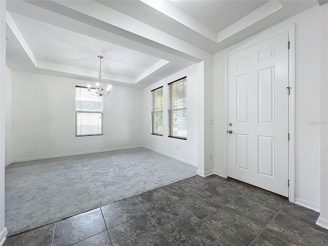 foyer with a raised ceiling, a notable chandelier, and dark colored carpet