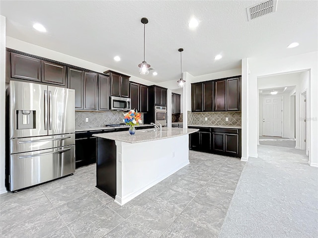 kitchen featuring tasteful backsplash, pendant lighting, stainless steel appliances, and a center island with sink