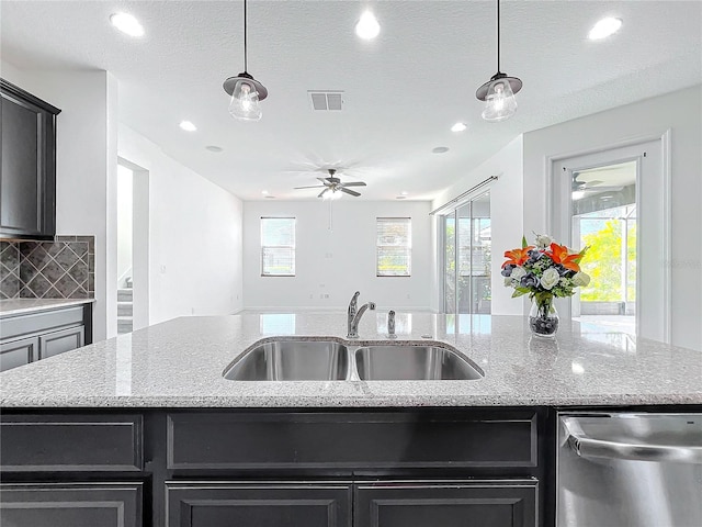 kitchen with stainless steel dishwasher, hanging light fixtures, sink, and a kitchen island with sink