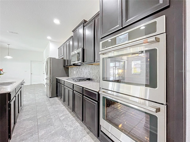 kitchen featuring pendant lighting, sink, decorative backsplash, a textured ceiling, and appliances with stainless steel finishes