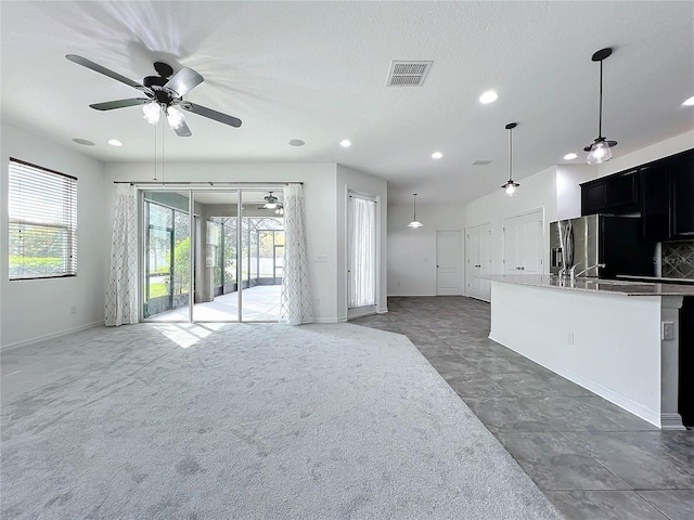 interior space with ceiling fan, a healthy amount of sunlight, stainless steel refrigerator with ice dispenser, and dark carpet