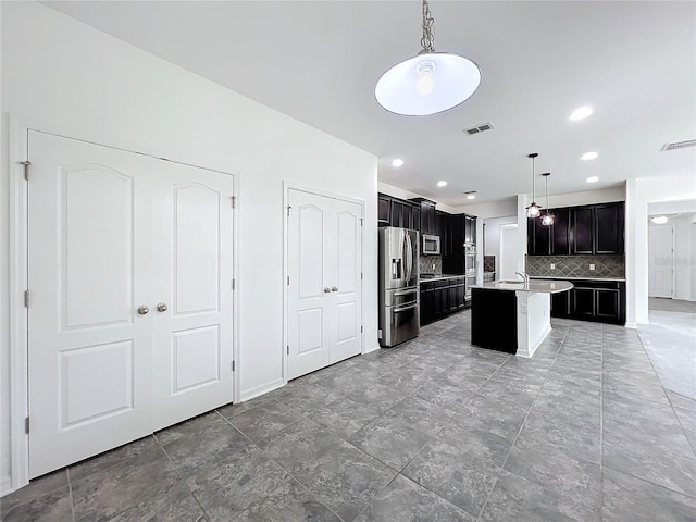 kitchen with backsplash, a center island with sink, appliances with stainless steel finishes, decorative light fixtures, and a kitchen bar