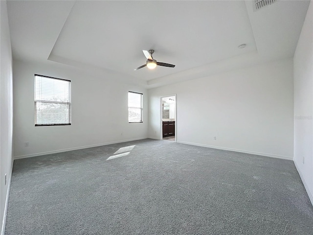 carpeted spare room with plenty of natural light, ceiling fan, and a raised ceiling