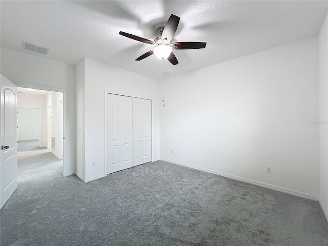 unfurnished bedroom featuring ceiling fan, a closet, a textured ceiling, and dark colored carpet