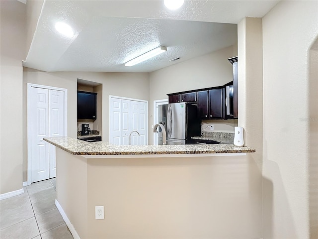 kitchen featuring kitchen peninsula, light stone counters, vaulted ceiling, and stainless steel fridge with ice dispenser