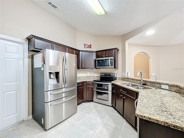 kitchen with light stone counters, appliances with stainless steel finishes, sink, and dark brown cabinets