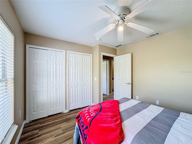 bedroom with dark hardwood / wood-style floors, multiple closets, a textured ceiling, and ceiling fan